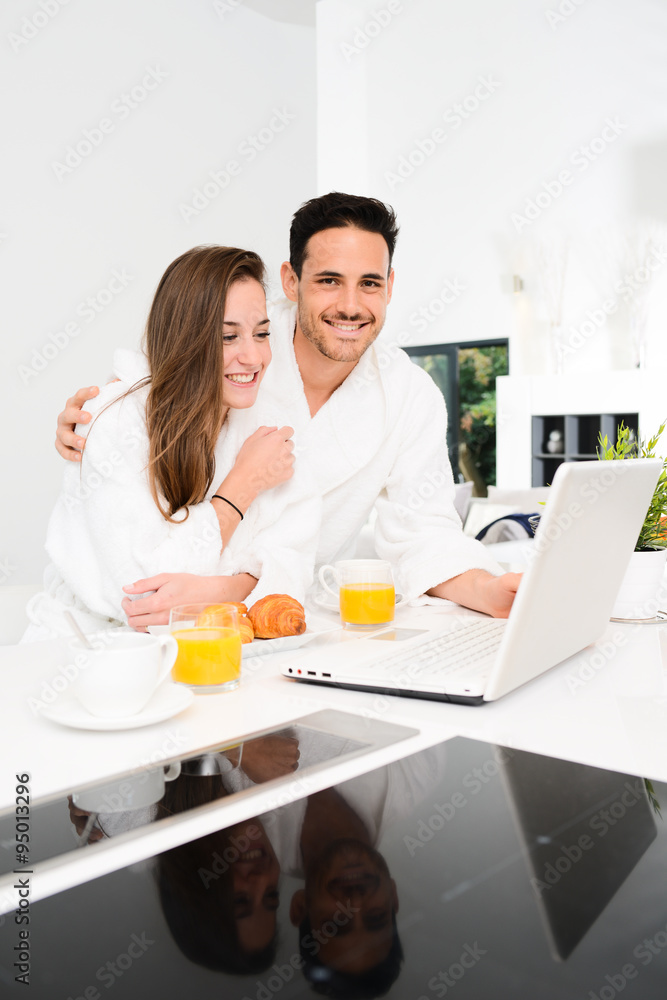 young couple in bathrobe at home having coffee in the kitchen and working on laptop computer young couple in bathrobe at home having coffee in the kitchen and working on laptop computer