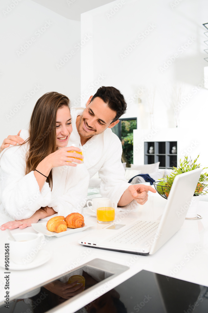 young couple in bathrobe at home having coffee in the kitchen and working on laptop computer young couple in bathrobe at home having coffee in the kitchen and working on laptop computer