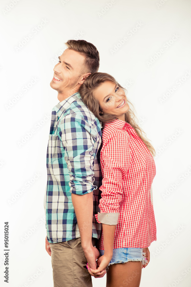 Happy couple in love holding hands standing back to back Happy couple in love holding hands standing back to back