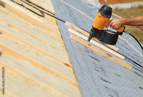 Building contractor worker (roofer) with a air nail gun nailer working on the roof on a new home constructiion project