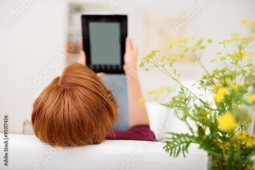 frau liegt entspannt auf dem sofa und liest etwas am tablet