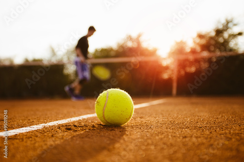 Fotografi Tennis ball and silhouette of player on a clay court