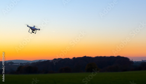 Unbemannte RC Drohne fliegt auf einem freien Feld bei Sonnenuntergang photo