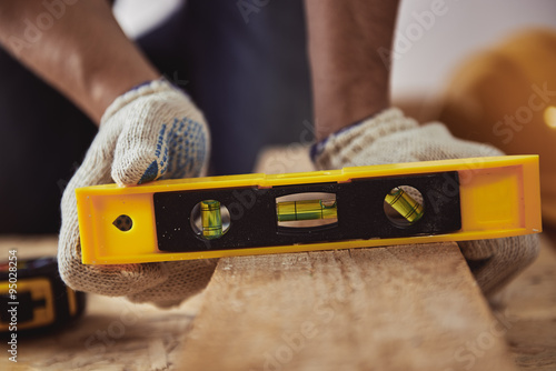 Male carver checking level of wooden plank in his shop. Construction concept. photo