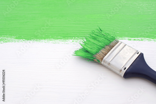 Paintbrush with green paint, painting over white board