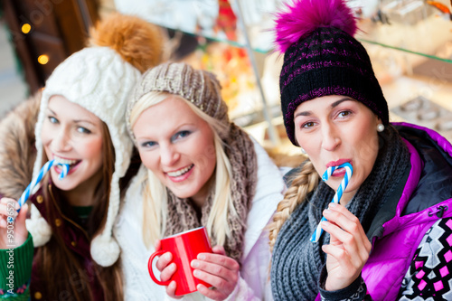 Frauen trinken Glühwein und essen Zuckerstangen auf deutschen Weihnachtsmarkt