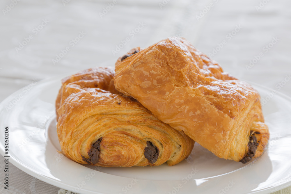 croissants with chocolate filling on a white plate, French pastries with a glass of orange juice in the background. side and top view, backlit, high-key.