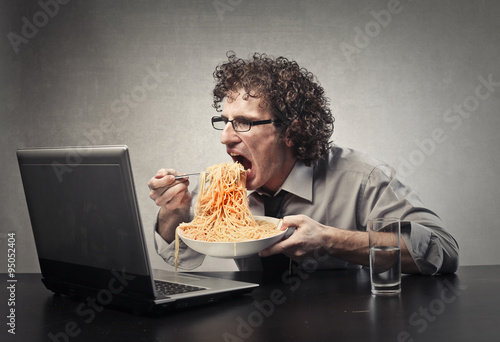 Man eating a huge dish of pasta in front of her laptop