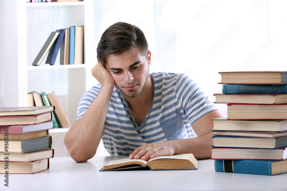 Young man reading book at table in room Young man reading book at table in room