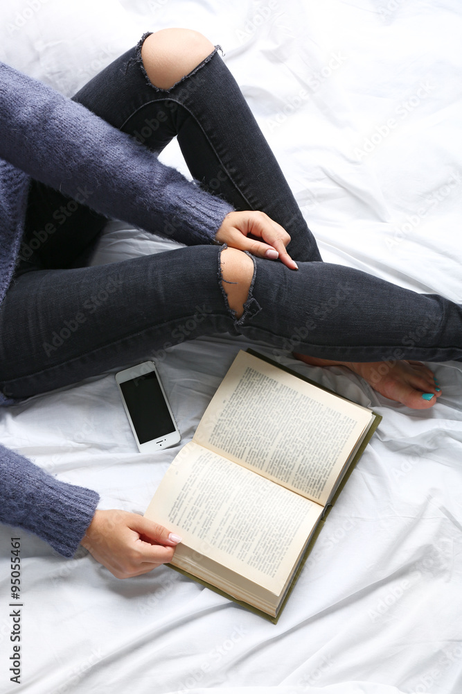 Obraz premium Woman in black jeans reading book on bed top view point