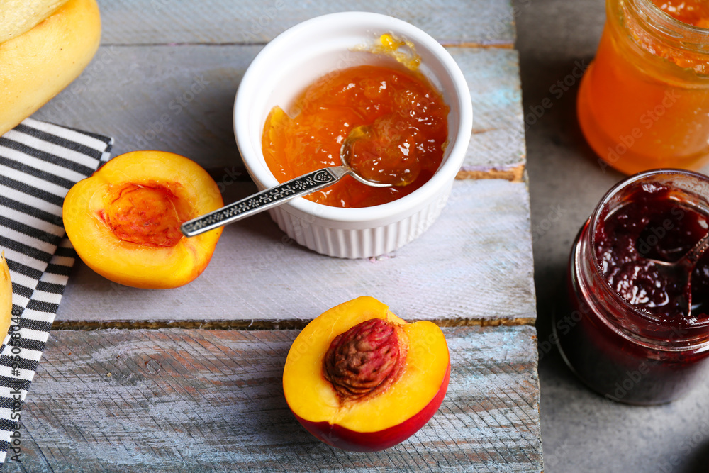 Tasty jam in the jar and bowl, ripe peaches and fresh buns on wooden background close-up Tasty jam in the jar and bowl, ripe peaches and fresh buns on wooden background close-up