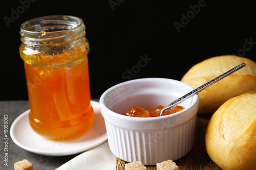 Tasty jam in the jar and bowl, crackers and fresh buns close-up