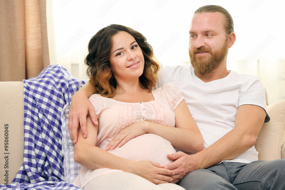 Happy beloved couple in waiting for baby's birth on sofa in the room Happy beloved couple in waiting for baby's birth on sofa in the room