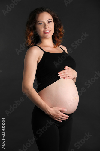 Young happy pregnant woman on black background