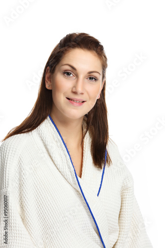 An attractive woman in her 20s sitting down wearing a white bathrobe smiling to camera. White background.