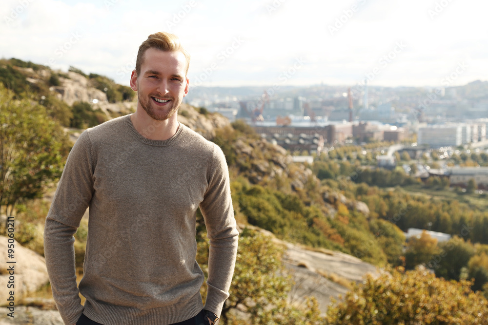 Trendy good looking man standing high up on a mountain with a great view of the city behind him on a sunny day. Trendy good looking man standing high up on a mountain with a great view of the city behind him on a sunny day.