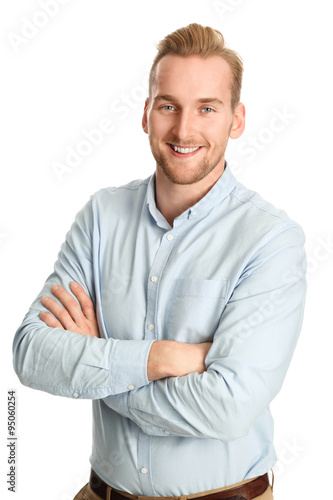 An attractive young man wearing a blue shirt with khaki pants, standing smiling towards camera against a white background. © _robbie_