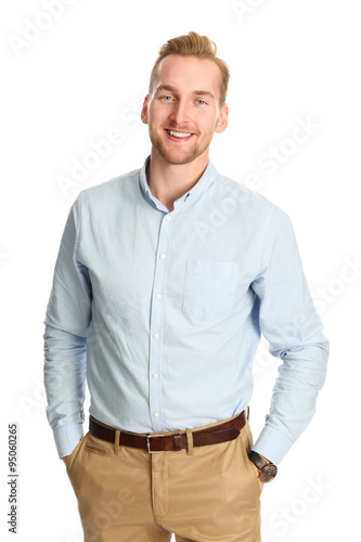 Fényképezés An attractive young man wearing a blue shirt with khaki pants, standing smiling towards camera against a white background
