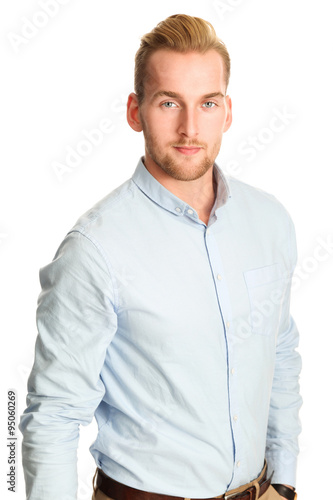 An attractive young man wearing a blue shirt with khaki pants, standing smiling towards camera against a white background.