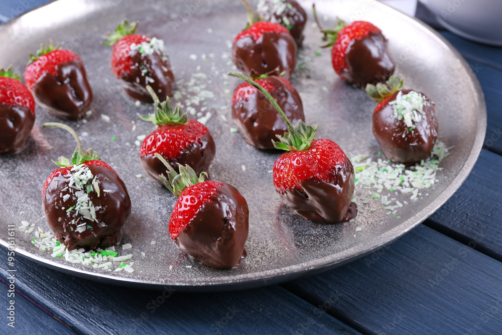 A plate of strawberries in chocolate on blue wooden background A plate of strawberries in chocolate on blue wooden background