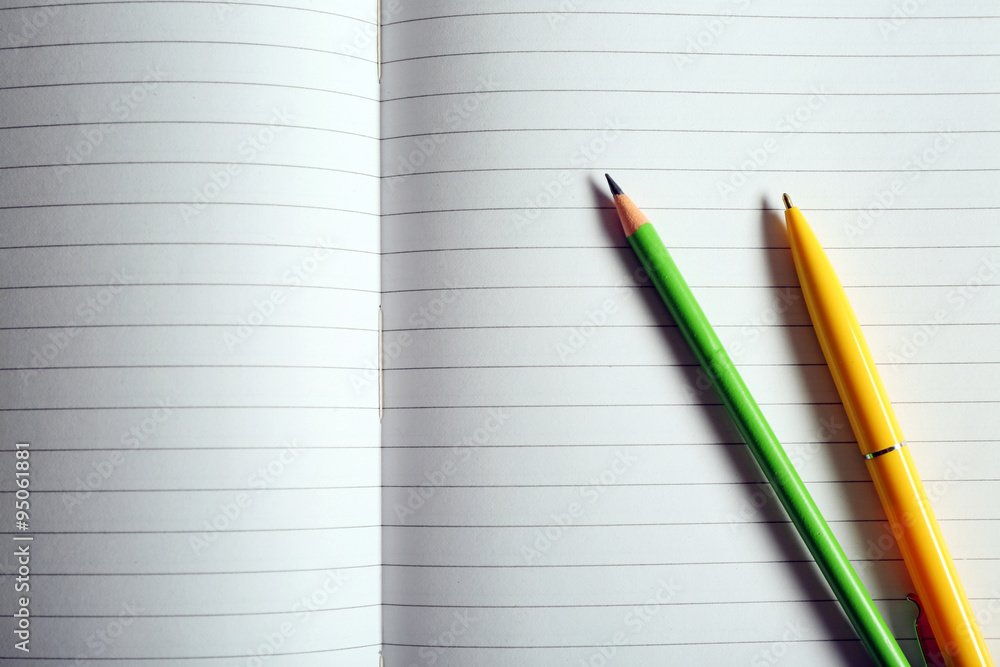 Opened striped note book background with yellow pen and green pencil Opened striped note book background with yellow pen and green pencil
