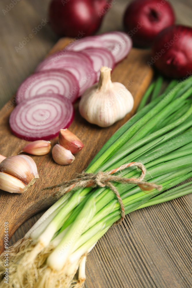 Red onions circles, green onion with garlic on board against wooden background Red onions circles, green onion with garlic on board against wooden background