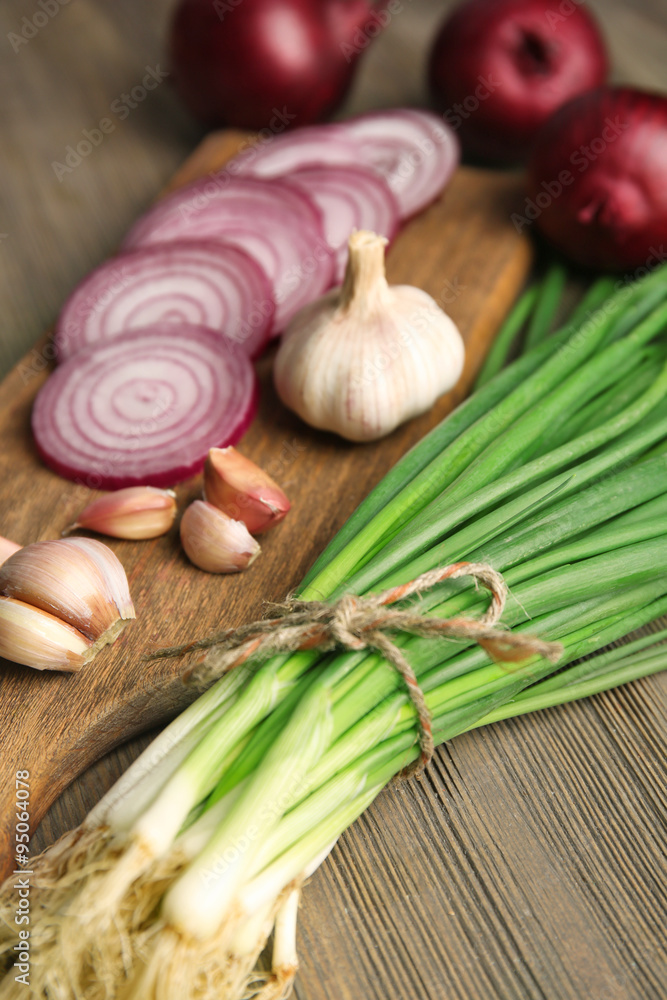 Red onions circles, green onion with garlic on board against wooden background