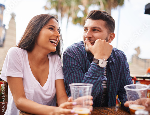Obraz na płótnie attractive hispanic couple drinking beer and having fun at outdoor restaurant