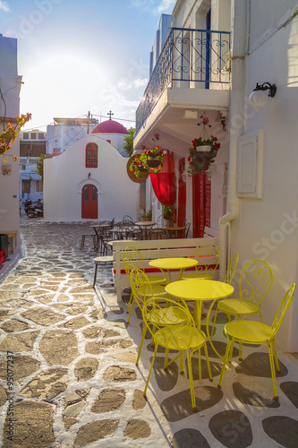 Mykonos streetview at sunrise with chapel and yellow chairs and tables, Greece © zgphotography