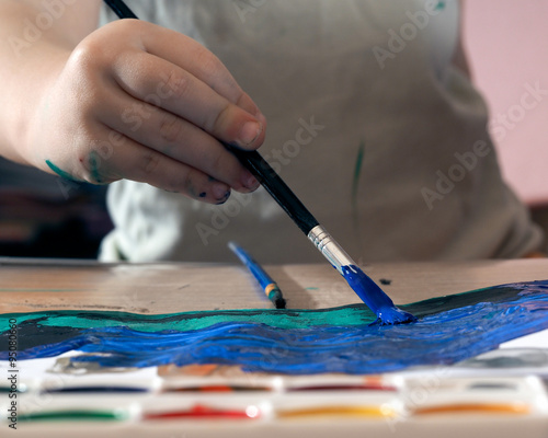 Ребенок рисует кисточкой и красками. Художник рисует синей краской море. Детский рисунок акварелью 