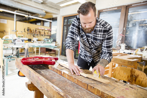 Carpenter sanding a wooden guitar neck in workshop