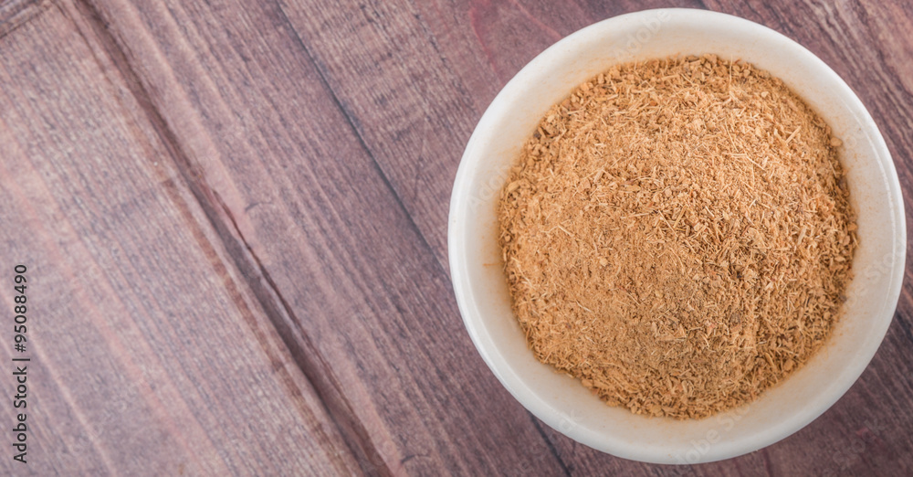 Dried galangal powder in white bowl over wooden background Dried galangal powder in white bowl over wooden background