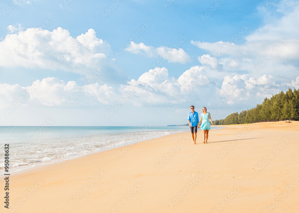 Couple walking on beach. Young happy interracial couple walking on beach smiling holding around each other.