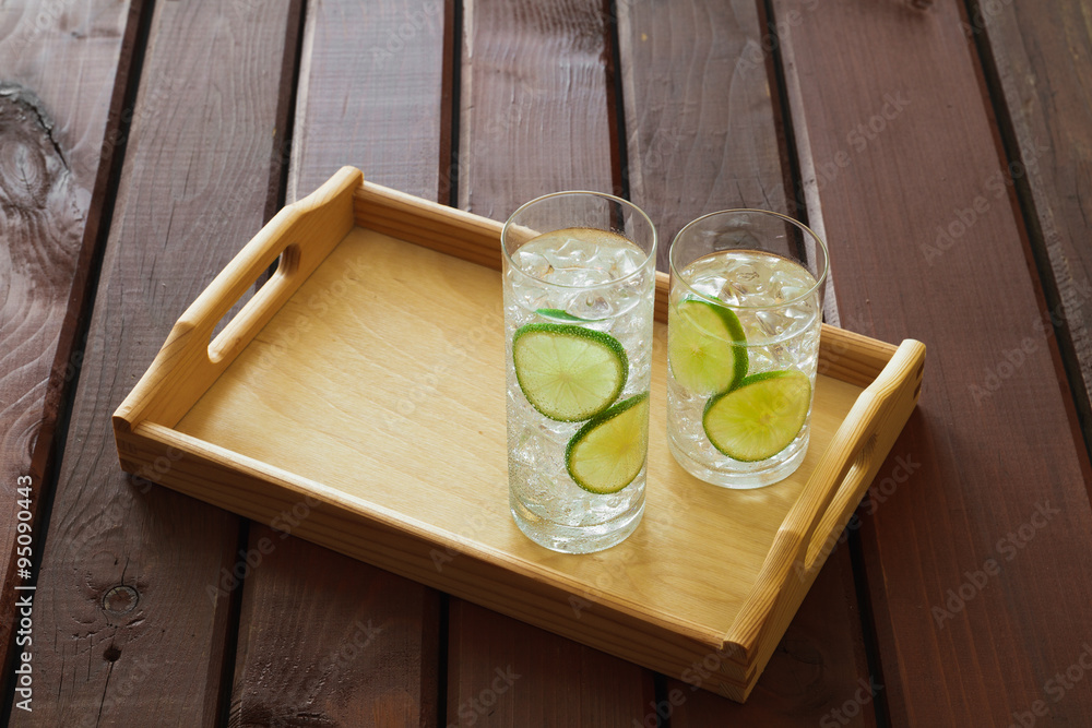 Two drinks on wooden tray with ice and condensation on glass