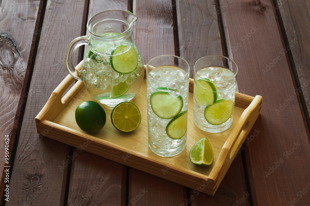 Two drinks and jug on wooden tray with ice and condensation on g
