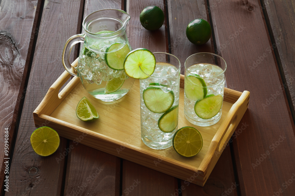Two drinks and jug on wooden tray with ice and condensation on g