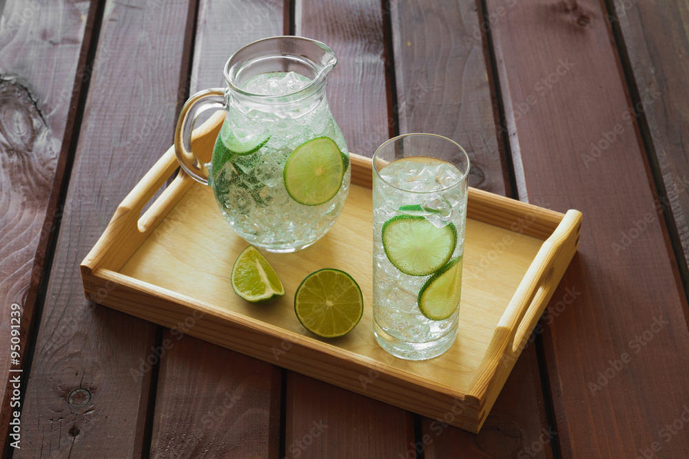 Drink and jug on wooden tray with ice and condensation on glass