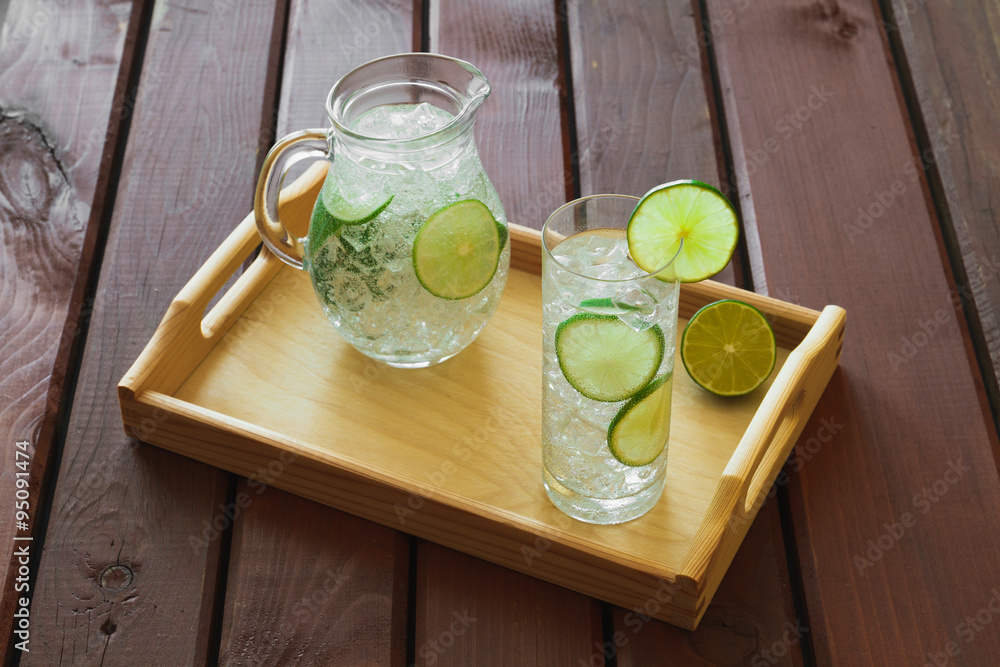 Drink and jug on wooden tray with ice and condensation on glass