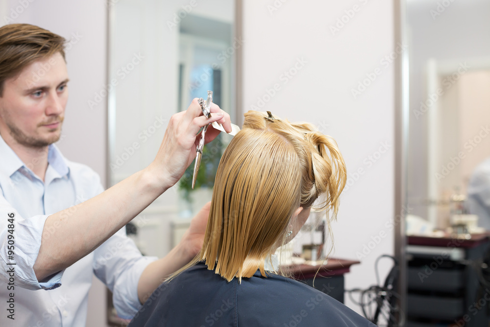 Handsome hairdresser making highlighting coloring and haircut of blonde female client Handsome hairdresser making highlighting coloring and haircut of blonde female client