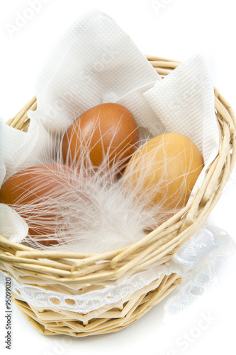 brown chicken eggs with white feather in a basket on a white