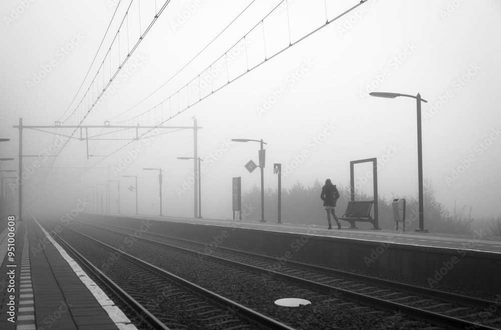Woman alone at a train station, waiting for the train on a foggy day in autumn.