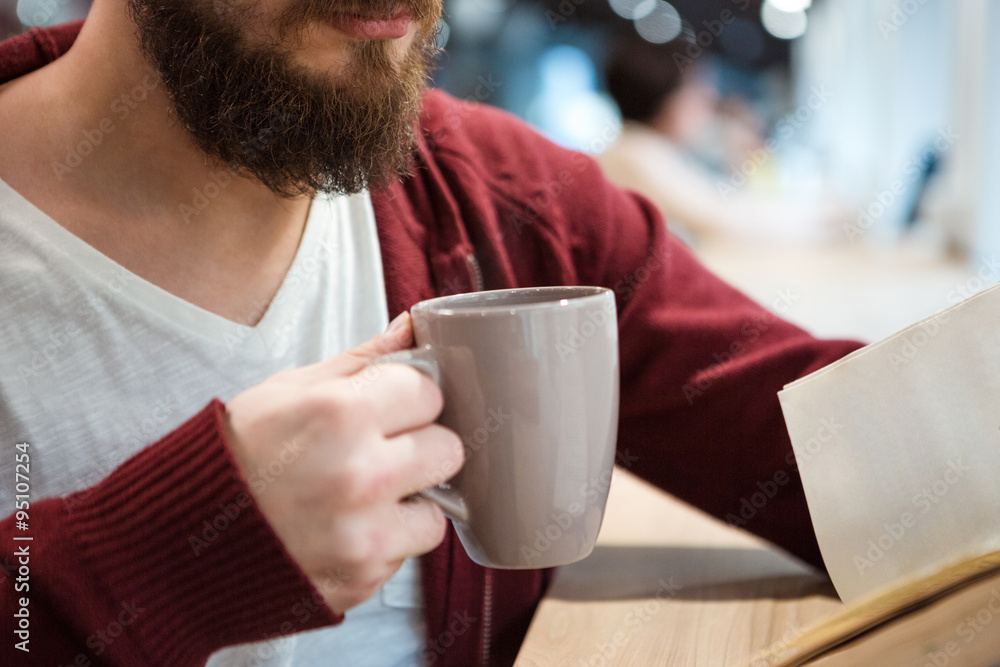 Young man holding a cup of hot drink and reading Young man holding a cup of hot drink and reading