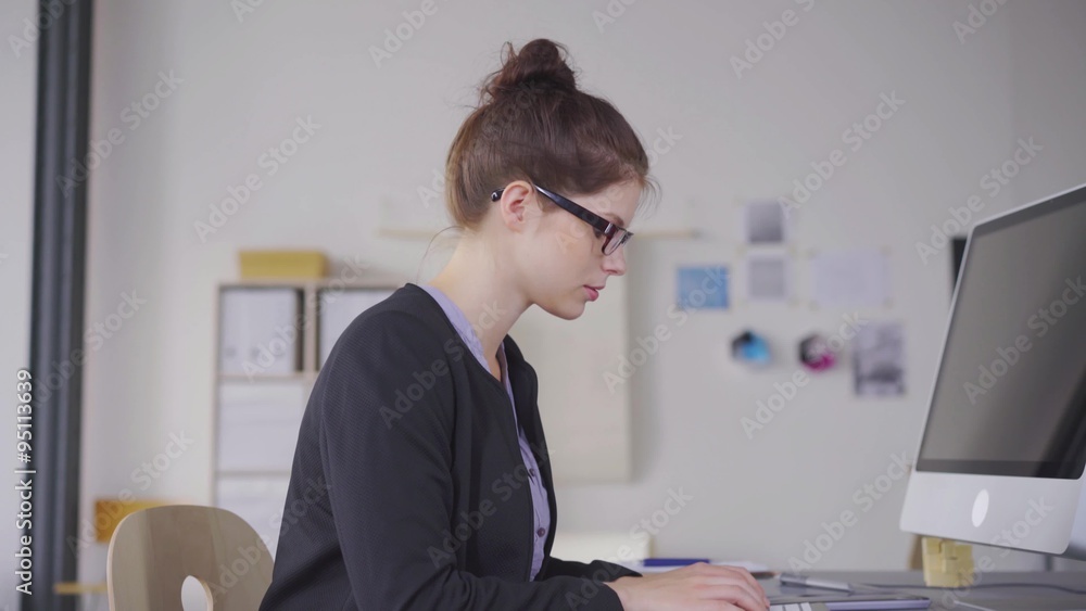 junge kreative mitarbeiterin in einem büro arbeitet am pc und streckt zufrieden die arme nach oben