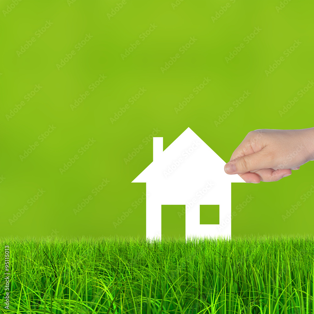Conceptual white paper house symbol held in hand in green grass Conceptual white paper house symbol held in hand in green grass