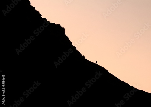 Lonely man climbing up to the mountain in sunset 