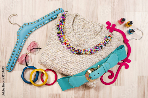 Winter sweater and accessories arranged on the floor. Woman colorful pink and blue accessories, hanger, belt, bracelets and nail polish. photo