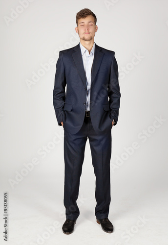 Young business man in dark grey suit stands confidently with hands in pockets.