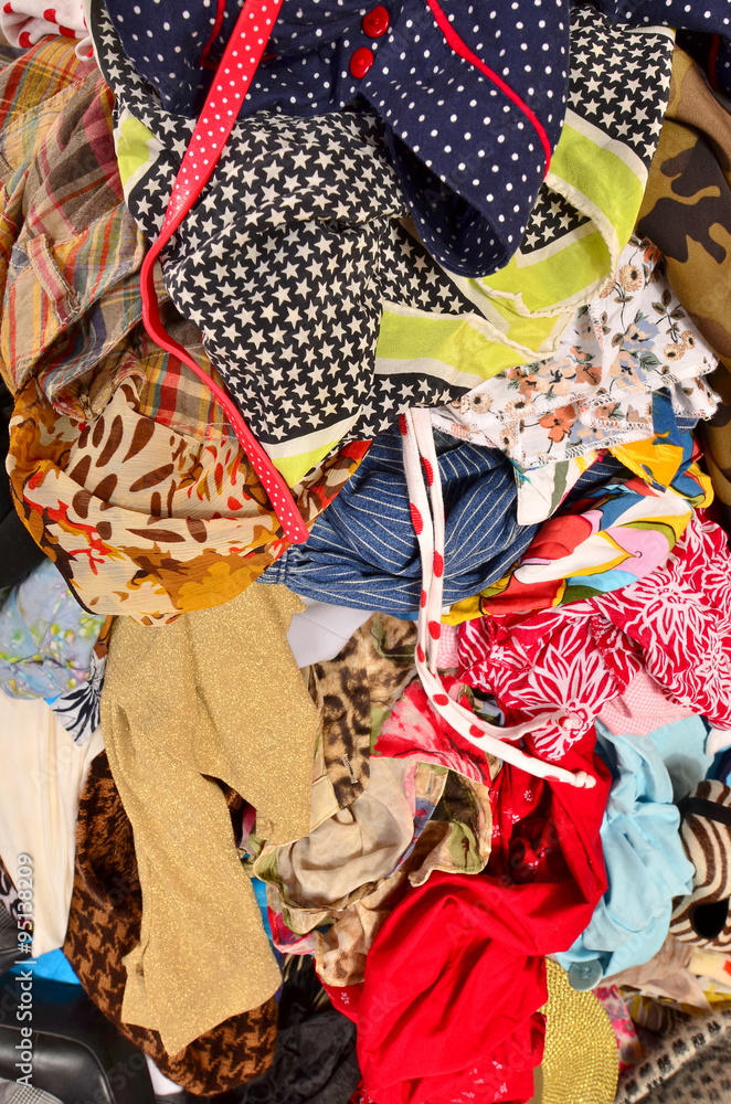 Close up on a big pile of clothes and accessories thrown on the ground. Untidy cluttered wardrobe with colorful clothes and accessories.