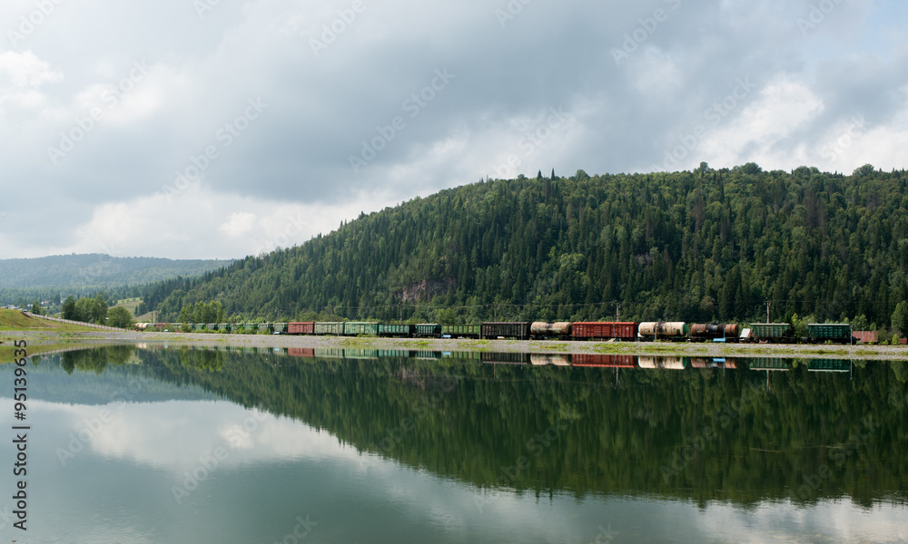 Railway vehicles among hills and with reflection in the lake