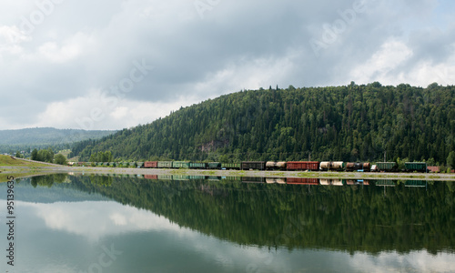 Railway vehicles among hills and with reflection in the lake